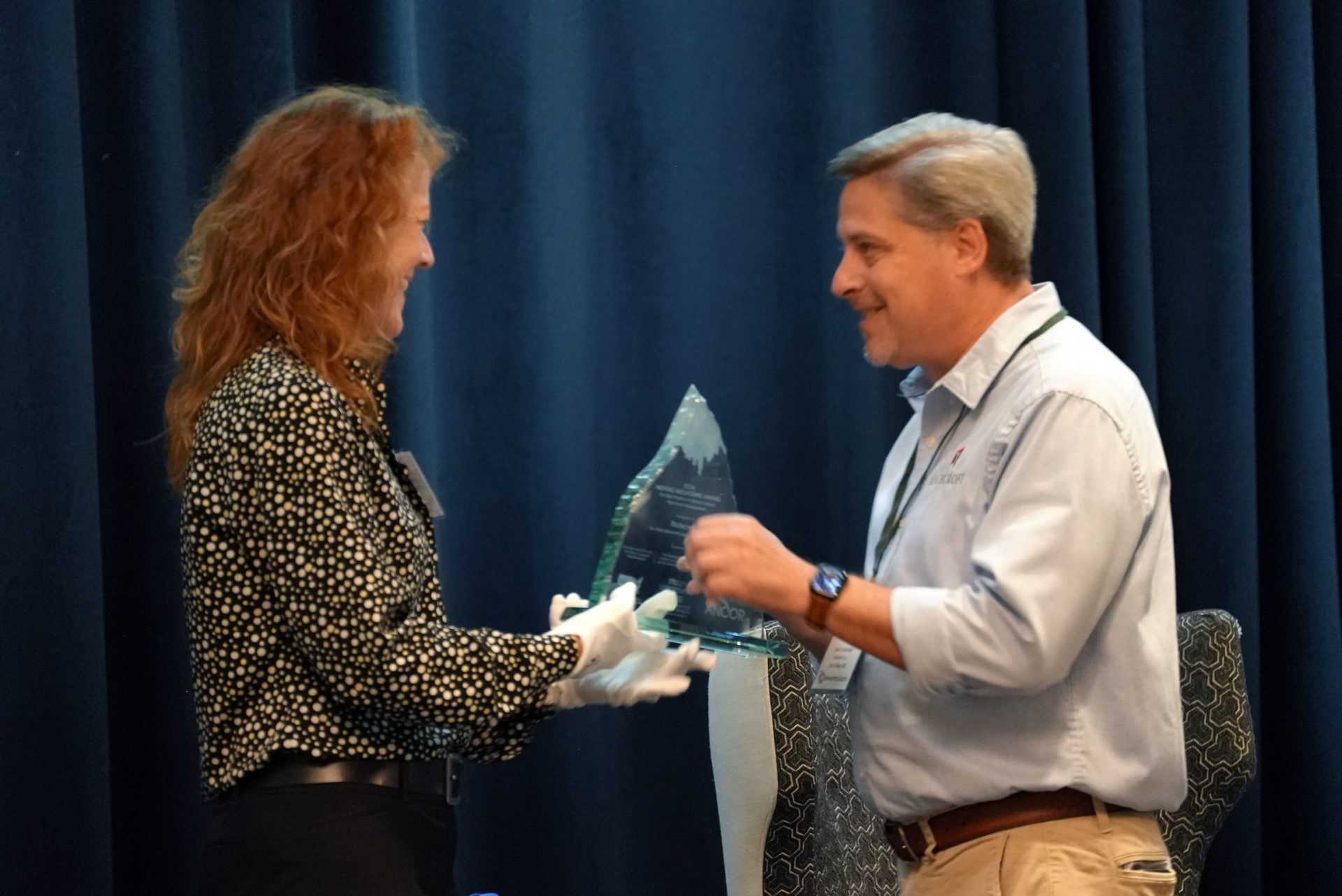 a woman hands a glass award shaped like a mountain to a man